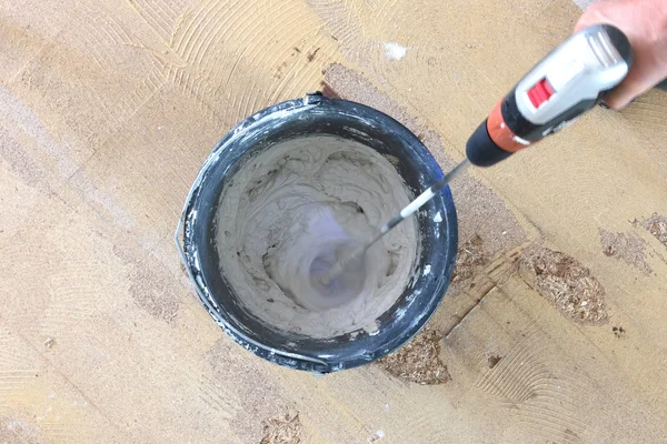 Adam matkap karıştırıcı elinde tutuyor. Adam gri beton ve baş kova içinde karıştırma.