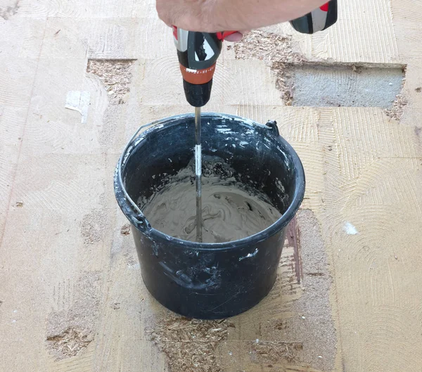 Adam matkap karıştırıcı elinde tutuyor. Adam gri beton ve baş kova içinde karıştırma.