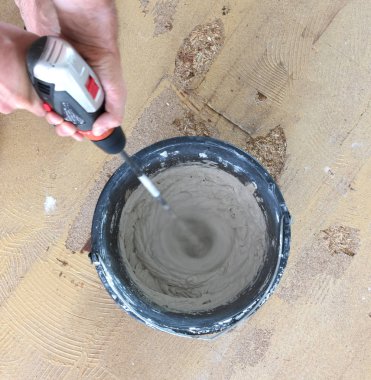 Adam matkap karıştırıcı elinde tutuyor. Adam gri beton ve baş kova içinde karıştırma.