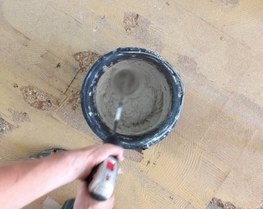 Adam matkap karıştırıcı elinde tutuyor. Adam gri beton ve baş kova içinde karıştırma.