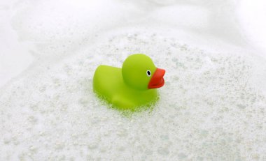 Küvette yeşil ördek, sabunla çevrili.