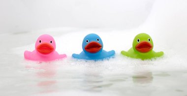 Küvette pembe, yeşil ve mavi ördek, sabunla çevrili.