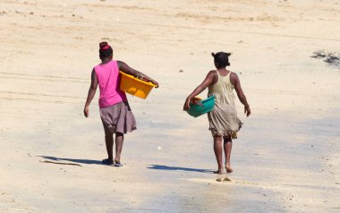 Afrikalı kadınlar sahilde çamaşırlarla yürüyorlar.
