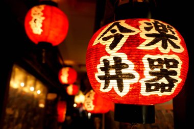 Osaka, Japonya, 16 Şubat 2018: Siyah Japon metinler üzerinde kırmızı kağıt fener bulanık arka plan ile gece zaman Japon restoranı saçak altında asılı.