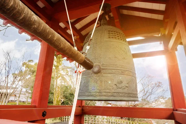 Büyük pirinç Budist çan ve darbe çan kereste parlak mavi gökyüzü güneş ve lens ile üzerinde kırmızı köşk içinde Japon tapınağın arka plan flare.