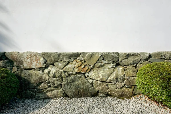 Crop of white and stone wall background with shadow shade of trees and gravel floor.