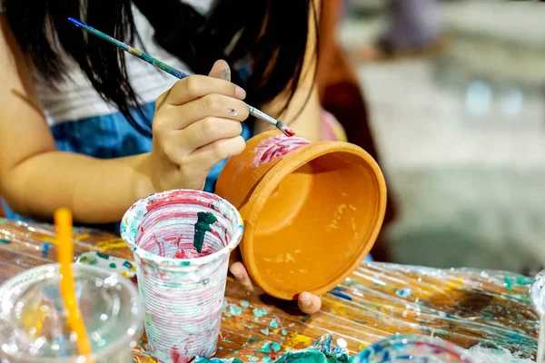 Asyalı küçük kız çalışma ve boya çiçek pot onun okulun sanat sınıfta öğrenme.