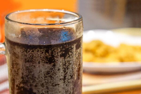 Крупный план и урожай черной газированной воды в стакане с пузырьками содовой и размытыми наггетсами на белом фоне.
.