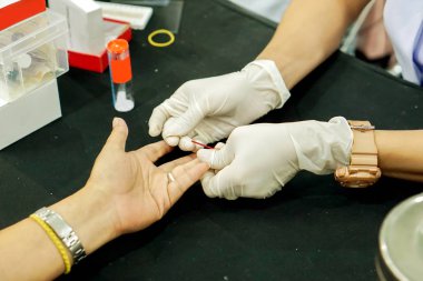 Hemşire elinde kılcal tüp kullanarak beyaz Medikal eldiven touch ve tıbbi klinikte kan şekeri kontrol etmek için insan işaret parmağı kan drenaj buna.