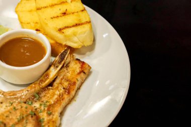 Portre ve t-bone siyah arka plan üzerine beyaz seramik plaka üzerinde biber soslu domuz eti biftek ve sarımsak ekmek izole kırpma.