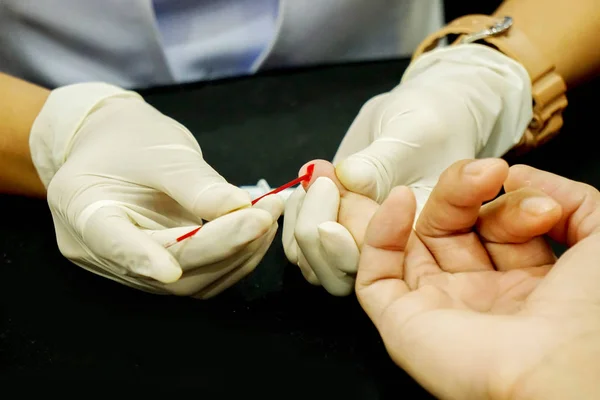 Eller hemşire kılcal tüp kullanarak beyaz Medikal eldiven touch ve insan yüzük parmağı tıbbi klinikte kan şekeri kontrol etmek için kan drenaj buna.
