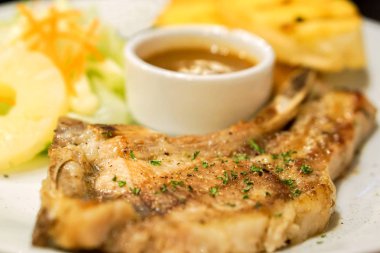 Portre ve kırpma t-bone domuz biftek ve sarımsak ekmek, beyaz seramik plaka üzerinde biber soslu salata süslemeleri ve ekrana sığdır.