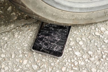 Closeup black mobile phone accident fall to the road and hit by motorcycle with glass broken on road background. clipart