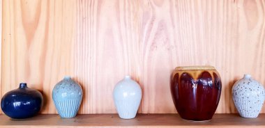 Ahşap raf ve duvar arka plan üzerinde çeşitli seramik vazo ve çiçek pot süslemeleri.