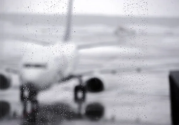 雨濡れた滑走路の背景に白い飛行機とターミナル空港の窓に雨滴のぼやけた画像モノクロ — ストック写真