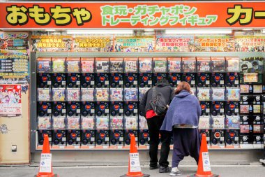 Osaka, Japonya-18 Ocak 2019 : Çinli çiftler, Den Den kasabasındaki oyuncak mağazasıgashapon'un keyfini çıkarıyor ve oynuyorlar. Gashapon Japonya'da popüler otomat makinesi dağıtılan kapsül oyuncaklar biridir.