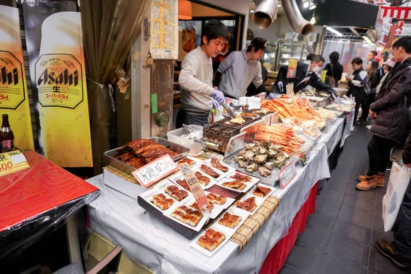 Osaka, Japonya, 16 Ocak 2019: Kuromon pazarında bekleyen müşteriler için iki genç aşçının peynirli deniz tarağı pişirdiği küçük bir sokak deniz ürünleri restoranı.