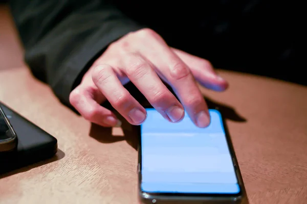 Hand of human play and touching his mobile phone on wooden table with bright lights of cafe.