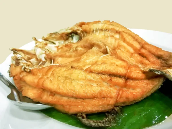 バナナの葉の上に魚の醤油とステンレススプーンの白いセラミックプレートをトッピングした揚げスナッパー魚 この料理はレストランで最も人気のあるタイ料理です — ストック写真