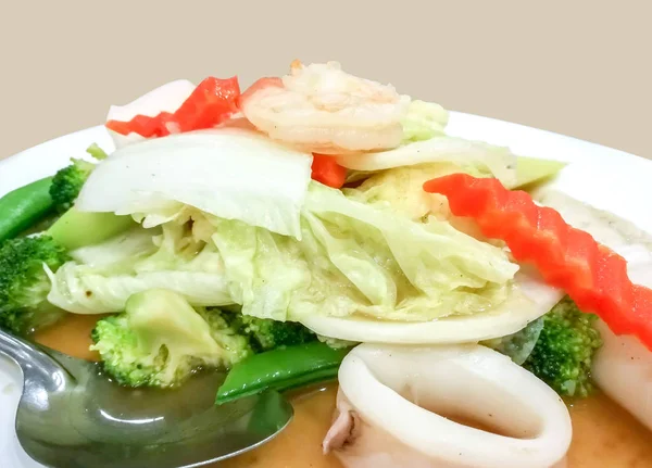 閉じるステンレススプーンと白いセラミックプレート上の魚介類と炒め野菜 — ストック写真