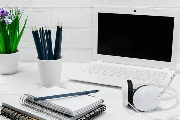 快適な職場のオフィス 空白の白いノートパソコンのヘッドフォンとノートブックとワークテーブル ホームオフィス デザイナー快適なワークスペース オフィスの机の電源とレンガのウールと光の背景に花 — ストック写真