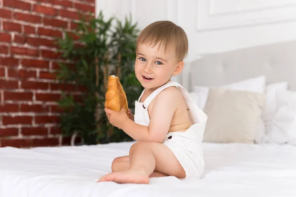 Retrato Feliz Niño Sonriente Jugando Comiendo Croissant Sentado Cama — Foto de Stock