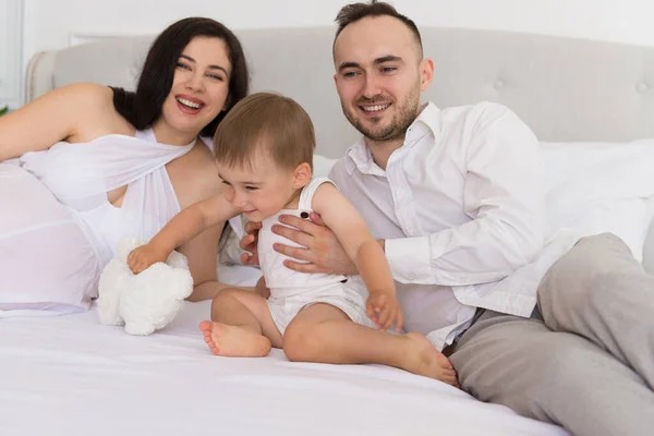 happy family on bed in the bedroom married couple with small child and pregnant woman