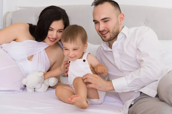 happy family on bed in the bedroom married couple with small child and pregnant woman