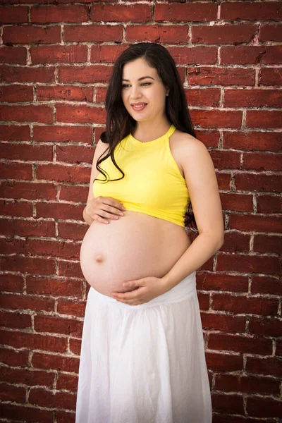 一个快乐的年轻孕妇站在砖墙旁边的画像 — 图库照片