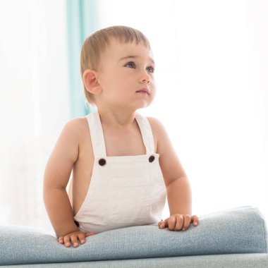 Beyaz tenli, gülümseyen bir çocuğun portresi. Oturma odasındaki kanepede oynayan bir çocuk.