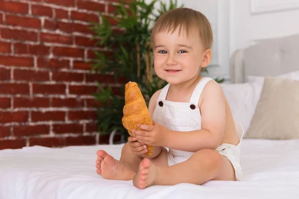 Iloinen Muotokuva Pieni Hymyilevä Poika Lapsi Pelaa Syö Croissant Istuu — kuvapankkivalokuva