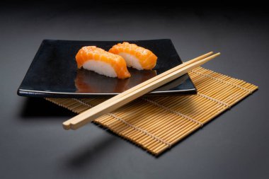 Somon suşi ve çubuk siyah arka plan üzerine siyah plaka