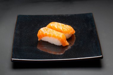 Siyah arka plan üzerine somon suşi ile siyah plaka