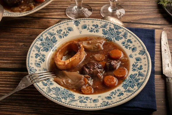 Well-cooked beef shank in wine sauce served in an antique plate on a wooden table