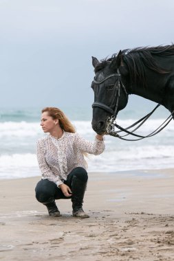 Bulutlu bir günde sahilde at üstünde genç bir kadın.