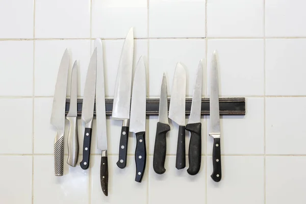 Collection of professional kitchen knives hanging on the wall with a magnetic bar