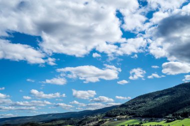 Panoramik ve dramatik doğa üzerinde kırsal dağ tepeleri üzerinde mavi bir gökyüzü çok bulutlu, pastoral tarım tarım arazileri, taze yeşil mera ve güneş ışığı ve tonlarında orman.
