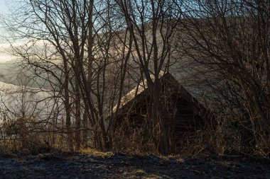 Atmosfer ve puslu sabah göl, dağ ve mistik küçük bir evi çıplak sonbahar ağaçları ile vahşi doğada üzerinde gündoğumu ile.