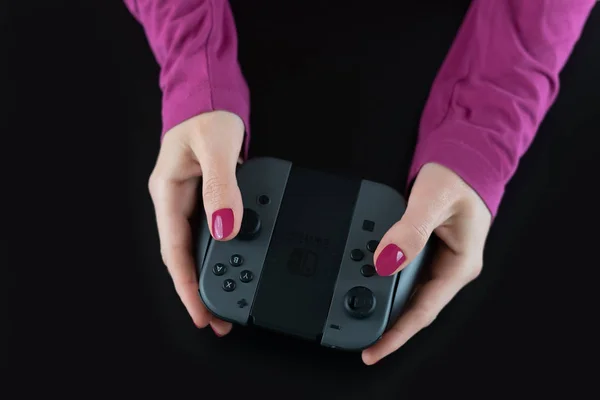 Pemandangan atas tangan wanita dengan cat kuku merah muda pada jari-jari yang memegang pengendali permainan Nintendo Switch untuk memainkan permainan video digital yang diisolasi hitam untuk hiburan hiburan bersenang-senang — Stok Foto