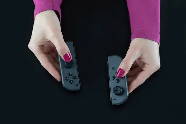 Vista superior de las manos de mujer con esmalte de uñas rosa en los dedos que sostienen los controladores de juego Nintendo Switch para jugar videojuegos digitales aislados en negro para divertirse entretenimiento de ocio —  Fotos de Stock