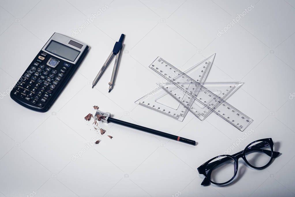 Top view of school supplies with calculator, paper compass, rulers, glasses, pencil and sharpener with wooden shavings - Concept of college student, university education, learning or high school
