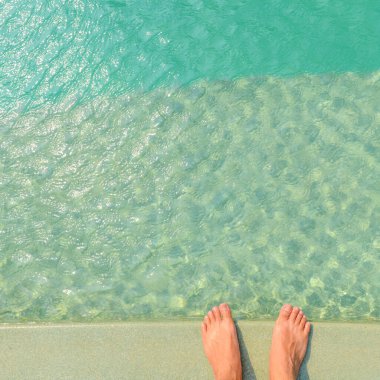 Adamın çıplak ayağı parlak mavi yüzme havuzunun kenarında duruyor, güneş ışığı yansımalı su, tatil, rahatlama, kaçış konsepti