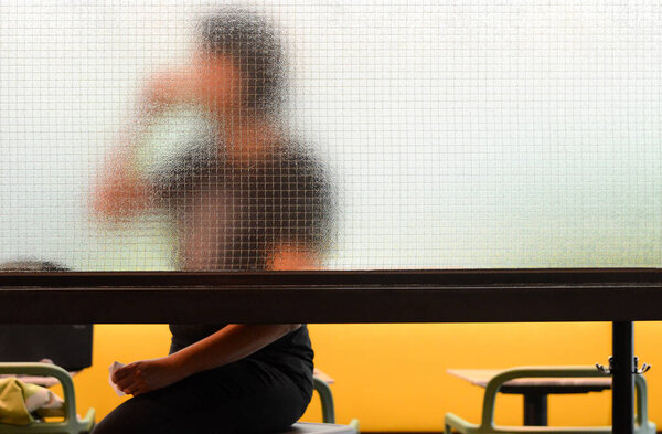 Woman is drinking coffee while sitting in modern coffee shop. Look through the mirror partition (silhouette)
