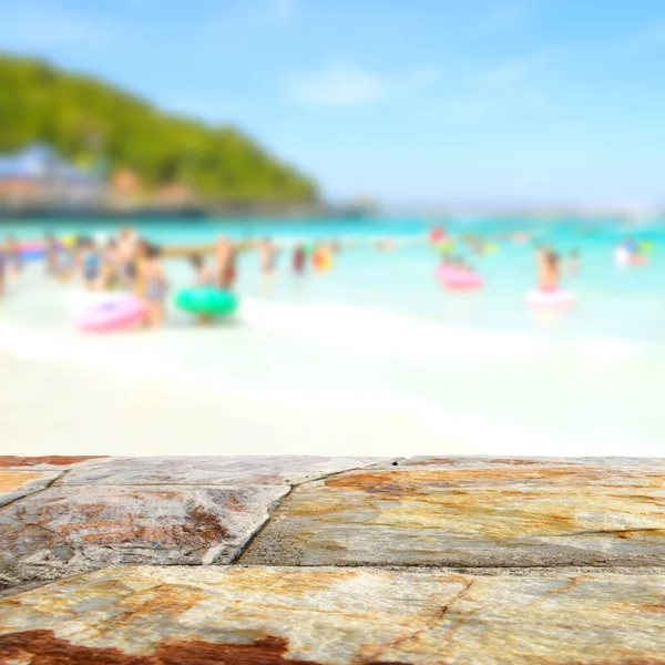 Kumsalda bulanık insanlarla kahverengi taş masa üstü, yaz tatili arka plan konsepti ürünlerinizi görüntülemek veya montajlamak için kullanılabilir