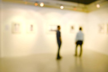 Sanat sergisi arka planı bulanık ve insanlar beyaz duvardaki resimlere bakıyor.. 
