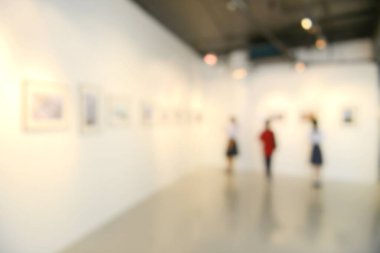 Sanat sergisi arka planı bulanık ve insanlar beyaz duvardaki resimlere bakıyor.. 