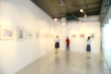 Sanat sergisi arka planı bulanık ve insanlar beyaz duvardaki resimlere bakıyor.. 
