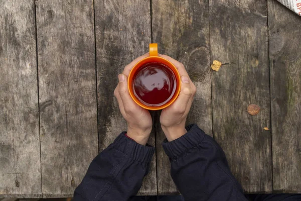 Vista superior de las manos de una mujer con manicura roja sosteniendo una taza de té sobre un fondo de madera — Foto de Stock