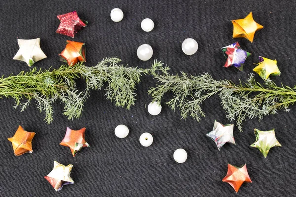 Estrellas de papel, perlas blancas y rama de árbol de diferentes colores sobre un fondo negro — Foto de Stock