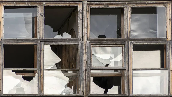 Gat in het raam glas door een kogel schot tijdens het schieten van de oorlog. Scheuren verspreid rond het gat. Groene bladeren van bomen wazig door het glas. Vuile raam frame. Uitzicht op een straat van binnenuit. — Stockfoto